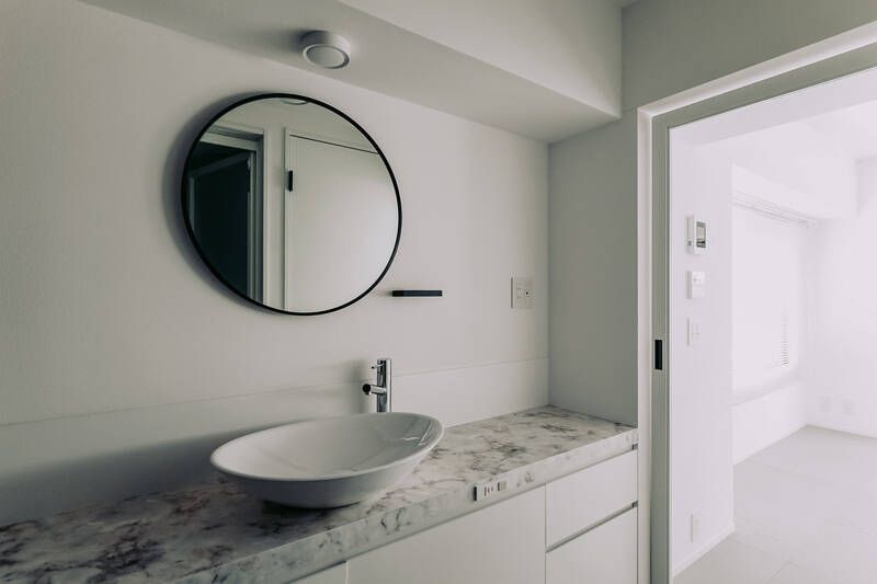 大理石調の洗面台に、オーバル型の洗面ボウルと円形のミラーが映える空間。