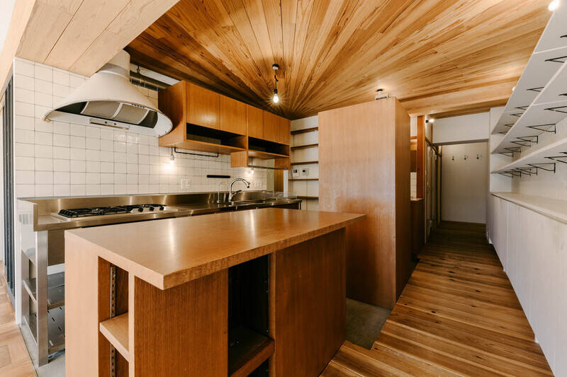 放射状に張られた天井のスギ板、ステンレスの作業台、レトロなデザインのレンジフード etc. が目を惹くキッチンです。床材は土間コンクリートに切り替わっています。