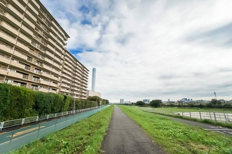 マンション（写真左手）裏手には、道路をはさんですぐ、多摩川の河川敷が広がっています。中央の水色の煙突は、隣の「多摩川清掃工場」のもの。音やにおいなど、気になりそうなところは特に見つかりませんでしたが、心配な方は現地にてご確認くださいませ。