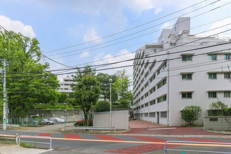 緑豊かな閑静な住宅街に佇む、白いマンション。1971年に大手ゼネコンによって建てられた、全3棟・総戸数184戸のビッグコミュニティです。敷地が広大なので入り口は2箇所にあり、こちらは「二子玉川」駅に近い、駒沢通りに面する入り口です。