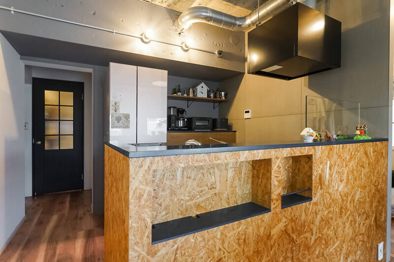 LDK中央の壁と同じくOSB材を使用したキッチン。カウンターやニッチに使われたモスグリーンの面材がアクセントに。ニッチの面材は外せる仕様で、中にはコンセントを設け、ケーブル類をすっきりと収納可能です。