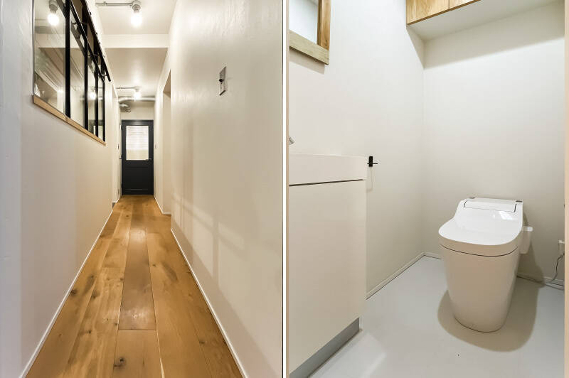 <b><b>左・</b></b>キッチンスペースの脇にある廊下。突き当たり左手の扉の先にトイレがあります。/<b><b>右・</b></b>トイレはタンクレスですっきりとしたフォルム。手洗い器付きです。
