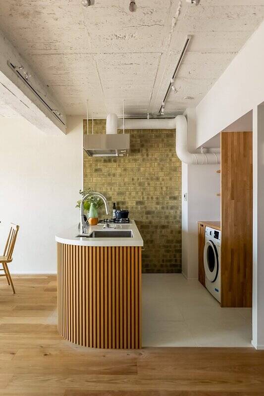 腰壁のリブ材やムラのあるタイル壁がさりげないアクセントに。台下はスペースが空いているので、ワゴンなどを用意するとよさそう。背面には洗濯機が収まっています。