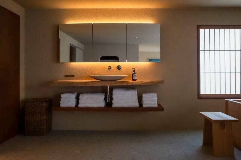 檜風呂の横に設けられた洗面台。間接照明の光が、壁の質感を引き立てています。また写真には写っていませんが、左手にトイレとシャワースペースもあります。