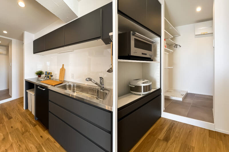 シンクは壁付けになっており、フロントオープンタイプの食洗機が備わっています。奥に家電置き場兼パントリー、さらに奥に洗濯機置き場と空間が連続しています。