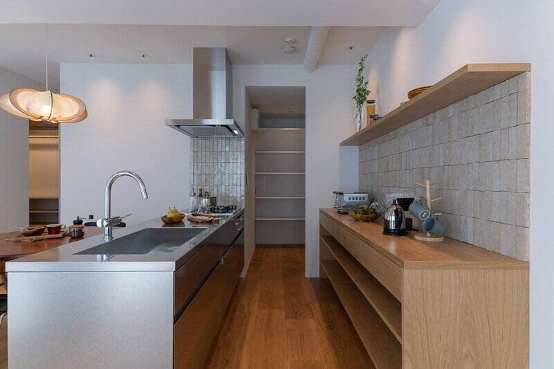 キッチンは3口コンロ付きで食洗機を完備。ステンレスの天板がフラットな美しいデザインで、LDKの雰囲気にスッと馴染んでいます。キッチン背面には棚を、奥には約1.7帖のパントリーを設置。