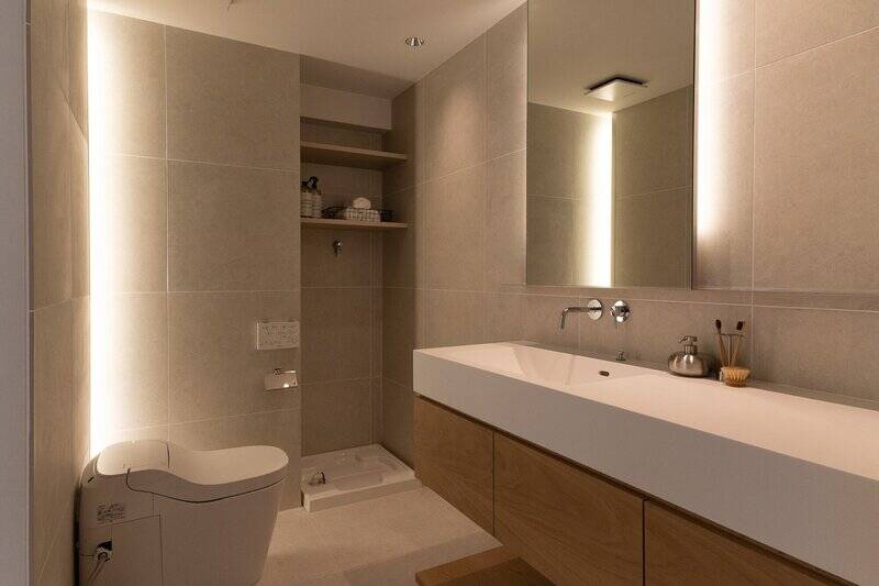 洗面台とトイレをまとめた、2in1のサニタリースペース。造作の広い洗面カウンターと間接照明を仕込んだミラーが、ホテルライクな高級感を演出しています。