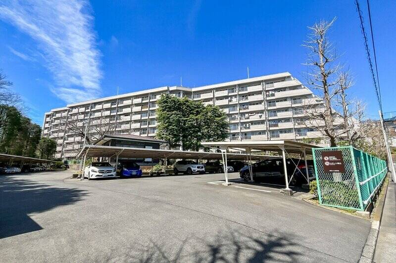 総戸数123戸のビッグコミュニティに到着! 1969年竣工と築年数は経過していますが、2002年にエレベーター棟の耐震改修工事、2020年に大規模改修工事を完了しており、適宜メンテナンスが行われてきたマンションです。建物手前には屋根付きの駐車場が広がっています。