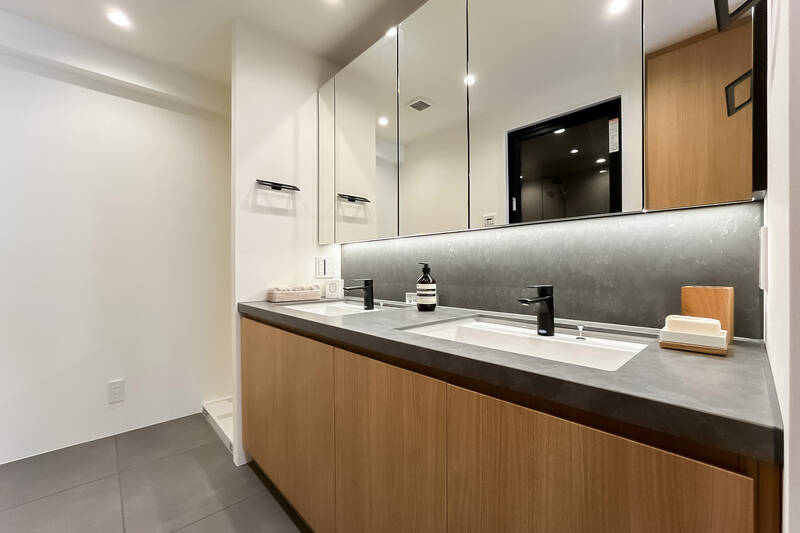 洗面化粧台はおふたり並んで使えるツーボウルタイプ。横に洗濯機置き場があり、背後にはリネン類をしまえる扉付き収納がありますよ。