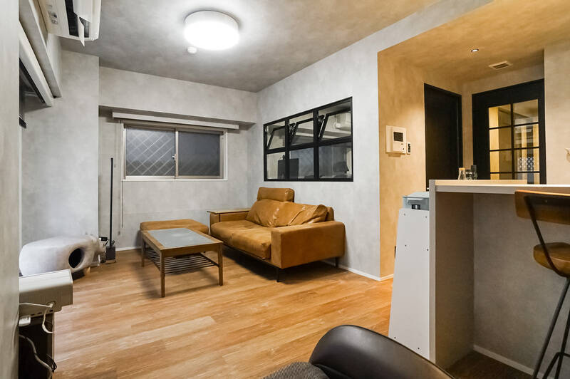 LDKの広さは約14.2帖。グレーのクロスに黒い建具で空間が引き締まっていて、かっこいい！ 室内窓の奥は洋室になっています。