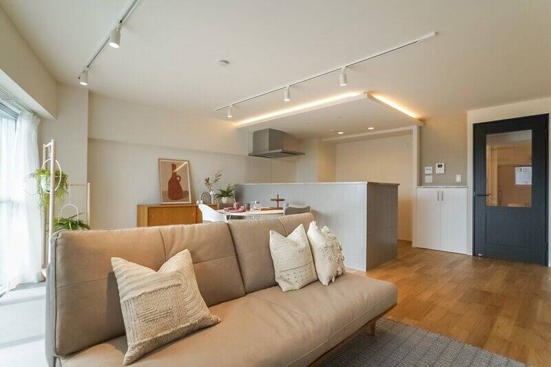 LDKはバルコニー側のラインが斜めになった形状で、写真手前が長く、奥にいくにつれて短くなるレイアウトです。キッチン上部は下がり天井になっており、縁に仕込まれた間接照明が空間をやわらかく照らします。