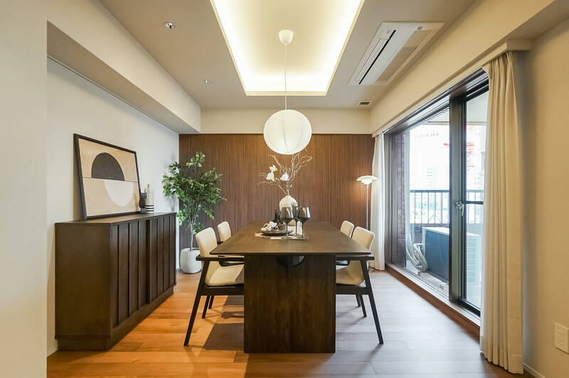間接照明を仕込んだ折り上げ天井やダウンライトが室内をほのかに照らし、大きなアートや観葉植物が似合う空間です。整って見えるように、エアコンはカセットタイプ（天井埋め込み型）を採用しました。