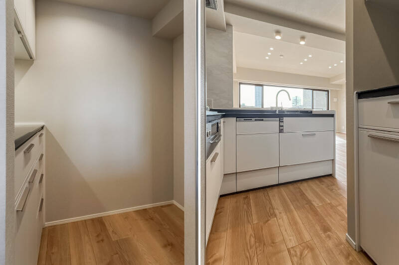 <p><b>左・</b>キッチンの奥には冷蔵庫スペースとカップボードが備わっています。必要なものが手の届く範囲にまとまり、家事動線がスムーズです。/<b>右・</b>シンク側からはLDの様子がよく見え、料理をしながらでも自然と会話が生まれそう。</p>