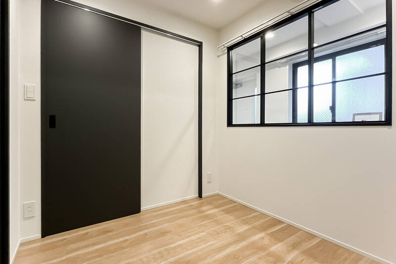 玄関土間とを隔てる室内窓が付いたコンパクトな居室です。写っていませんが、反対側の壁面にはグレーのクロスが貼られています。