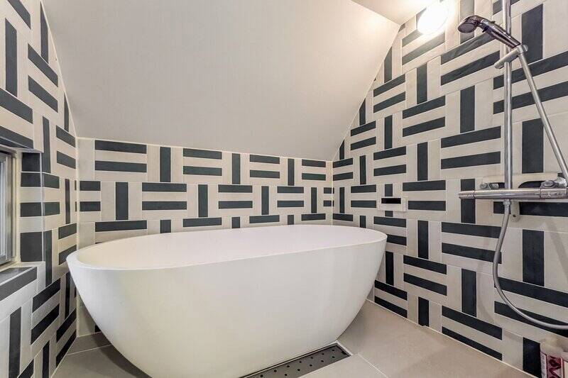 黒と白のタイルが縦横に規則正しく貼られたユニークな空間。置き型浴槽にオーバーヘッドシャワーが備わった、海外らしいスタイルのバスルームです。