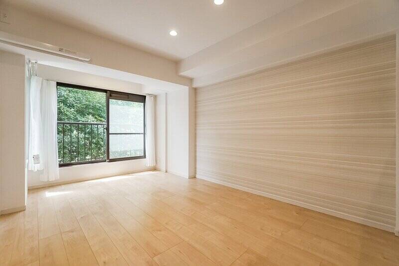 まずは約12帖のLDKから見ていきましょう。南西向きの窓の向こうには、植栽の豊かな緑が。右手の壁には、木目を思わせるナチュラルテイストのアクセントクロスがあしらわれています。