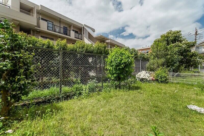 ツツジの咲く専用庭に出てみました。足元が芝生でフカフカです！ お向かいの建物とは距離が取れていますが、両隣の住戸の専用庭とは低い柵で区切られているだけなので、しっかりと目隠しするのは難しそう。声を掛け合いながら和やかに過ごすのが吉です。