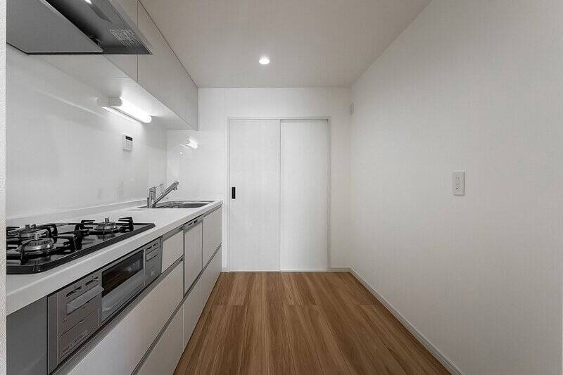 キッチンは壁付けのI型。食洗機に3口ガスコンロにグリル、吊り戸棚を含むたっぷりの収納を備えています。