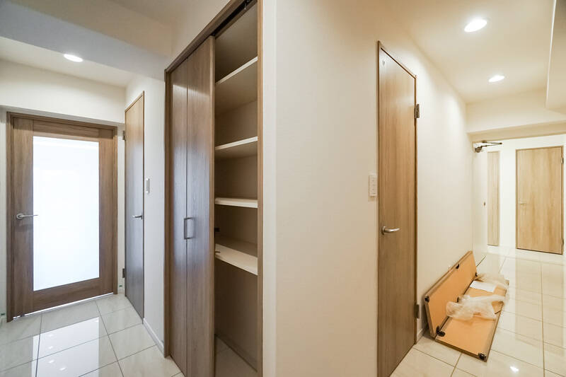 廊下に出て、角から全体を見渡したカット（右手に写っているのは残工事の資材です）。左がLDK、右手奥が玄関です。水まわり・トイレが住戸の中心にまとまっており、それを囲むように4つの洋室が並んでいます。順番に見ていきましょう。