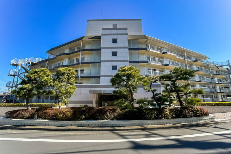 松の木越しの車寄せ、そして『おかえり！』と両腕を伸ばすように歓迎してくれるような建物。青空が似合うこちらのマンションの一室を今回はご紹介。（2022/09撮影）