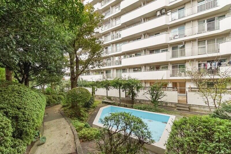 こちらは反対側、マンション敷地の植栽エリアから撮影しています。右手に、今出てきた住戸の専用庭が写っているのが分かるでしょうか？ なんとゲートを出ると、そこには共用施設の幼児用プール（使用細則あり）＆ベンチがありました。サマーシーズンにはここで水遊びができるかも！